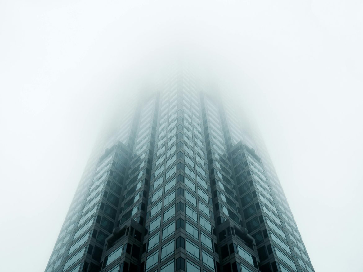 Glass skyscraper disappearing into fog