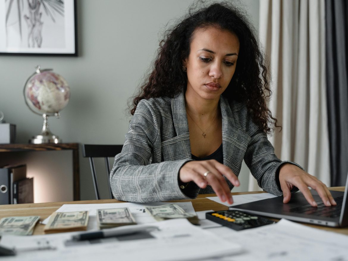 Businesswoman at a desk with cash, a calculator, and a laptop
